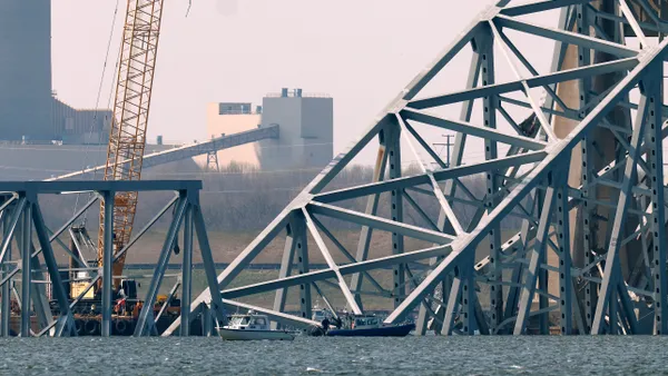 A yellow crane is dwarfed by massive broken steel debris from a bridge.